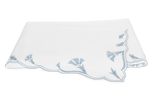 The Marcella Bedding Collection by Matouk in Hazy Blue features elegant scalloped edges and blue floral embroidery on a crisp white background.