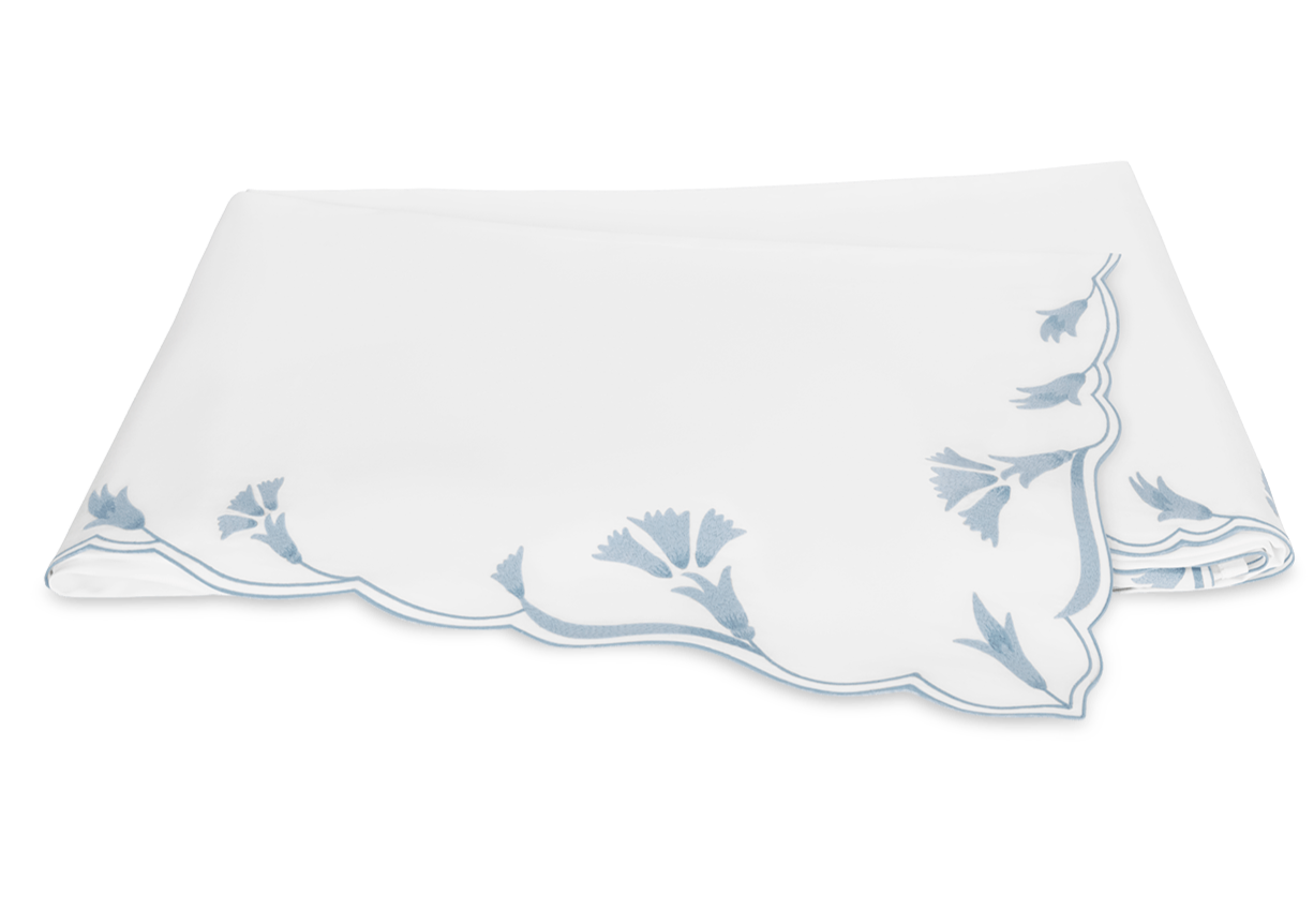 The Marcella Bedding Collection by Matouk in Hazy Blue features elegant scalloped edges and blue floral embroidery on a crisp white background.