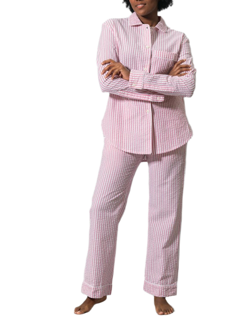A person stands barefoot with arms crossed, wearing the Matouk Matteo Pajama Set in classic pink-and-white striped seersucker cotton, set against a white background.