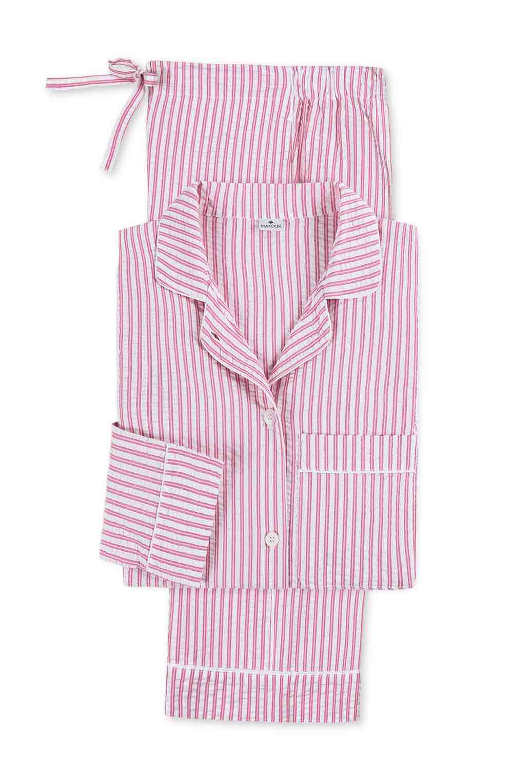 The Matteo Pajama Set by Matouk features pink and white seersucker cotton stripes, a button-up top with collar and breast pocket, plus a matching drawstring pouch—all laid out flat.