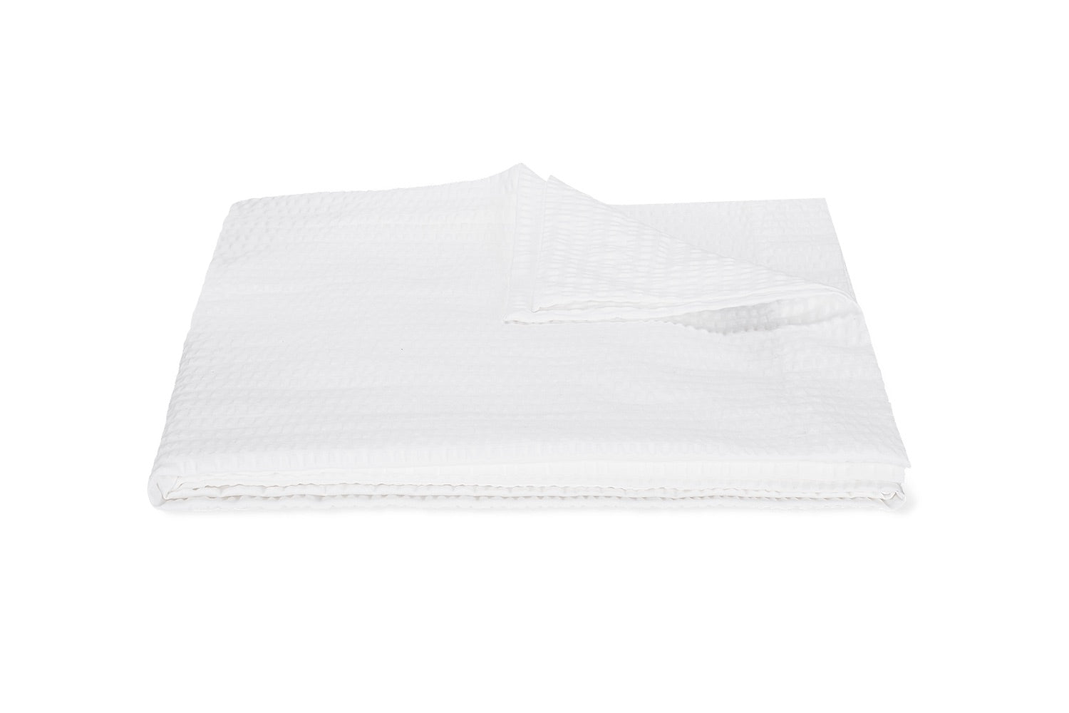 A neatly folded white blanket from the Matouk Matteo Bedding Collection, featuring a textured design reminiscent of seersucker, is displayed on a white background with one corner turned over.
