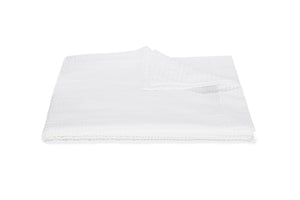 A neatly folded white blanket from the Matouk Matteo Bedding Collection, featuring a textured design reminiscent of seersucker, is displayed on a white background with one corner turned over.