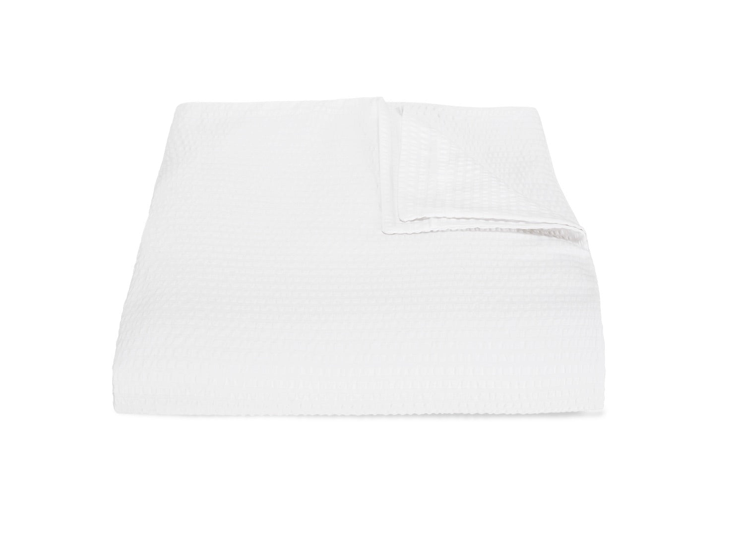 A neatly folded blanket from the Matouk Matteo Bedding Collection in white, with one corner gently turned over, is displayed against a plain white background.