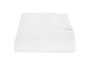 A neatly folded blanket from the Matouk Matteo Bedding Collection in white, with one corner gently turned over, is displayed against a plain white background.