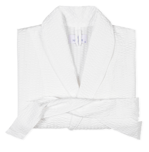 The Matteo White Robe by Matouk, featuring a lightweight waffle weave, shawl collar, and matching belt, is neatly folded on a plain background.