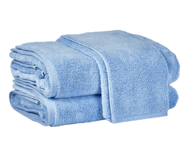 Two blue cotton towels from the Matouk Milagro Bath Collection, Azure, are neatly stacked, offering OEKO-TEX certified quality by Matouk for ultimate comfort.