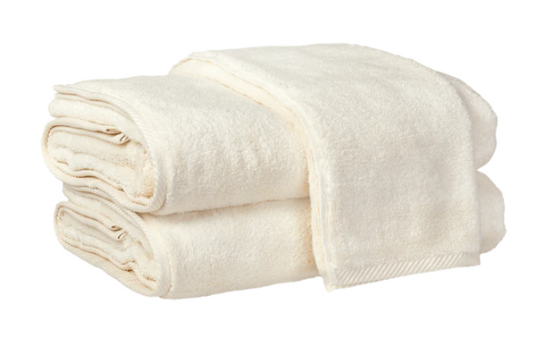 Two ivory towels from the Matouk Milagro Bath Collection, known for their softness and absorbency, are neatly folded and stacked against a plain white background.