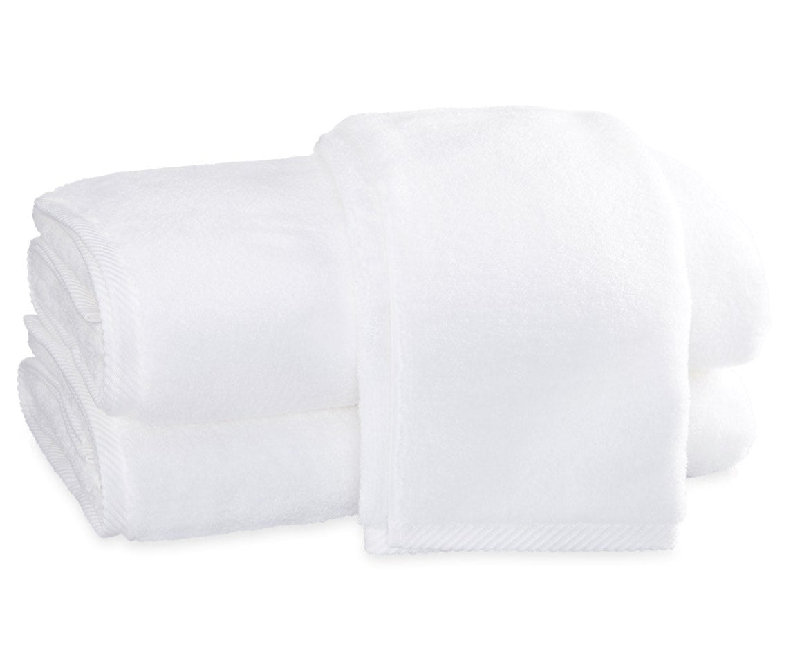 Two neatly folded white towels from the Matouk Milagro Bath Collection, crafted with zero-twist yarns, are stacked on a plain white background.