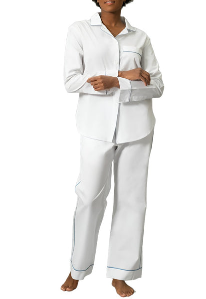 A woman wearing a Matouk Milano Pajama Set in white with blue piping, standing against a white background.