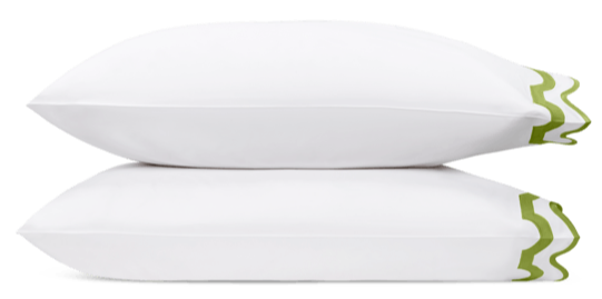 Two white pillows from the Matouk Mirasol Bedding Collection in Grass, featuring green wave-like trim on one edge, highlight the luxurious softness of Egyptian cotton percale against a plain background.