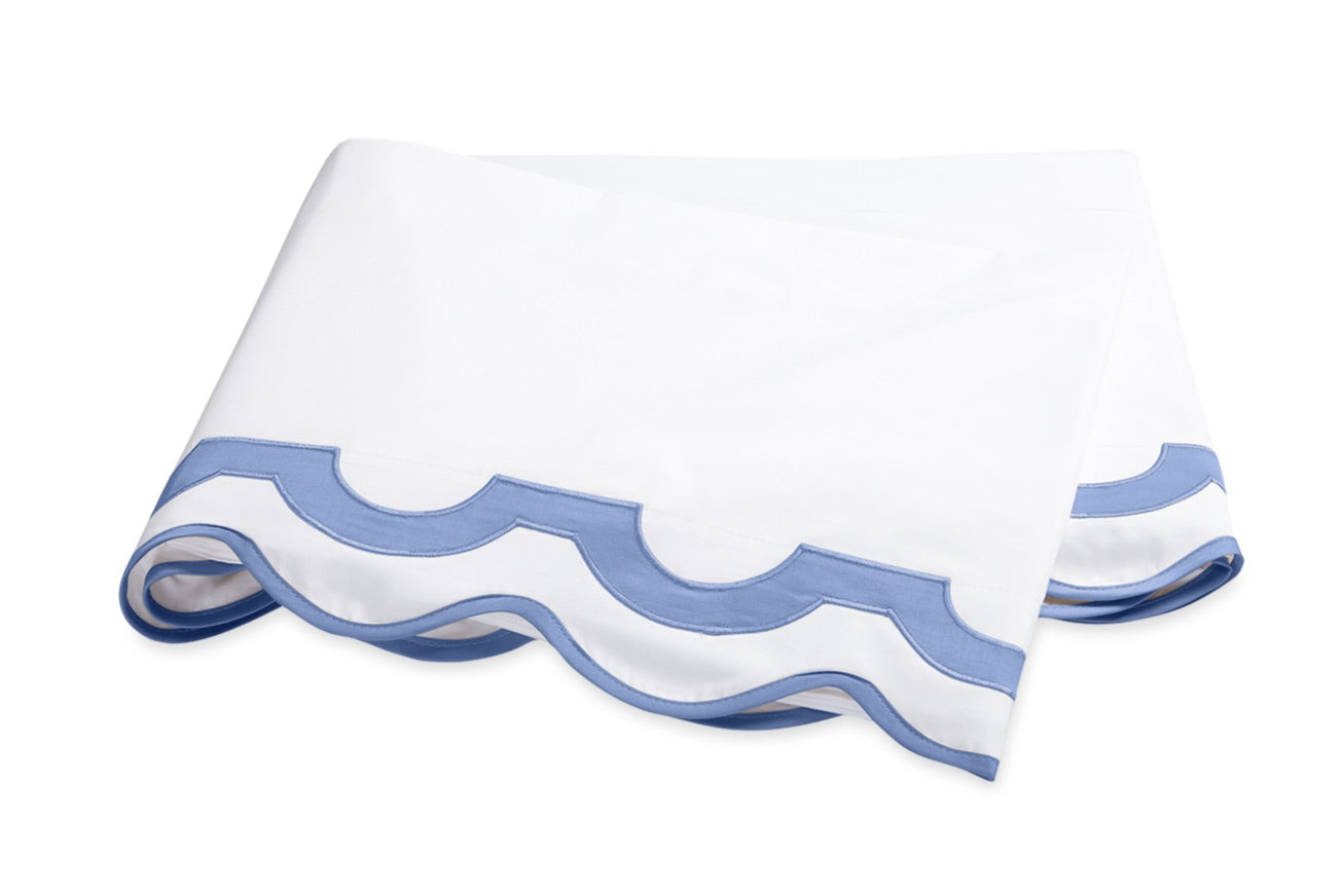 The Mirasol Bedding Collection by Matouk features a folded white sheet adorned with a light blue scalloped border, expertly crafted in Italy from luxurious 600 thread count Egyptian cotton percale, and showcased against a plain white background.