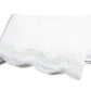 Showcasing the Mirasol Bedding Collection by Matouk, this folded white sheet features elegant scalloped edges and delicate light green trim, expertly crafted from luxurious Egyptian cotton percale with a 600 thread count, displayed against a plain white background.