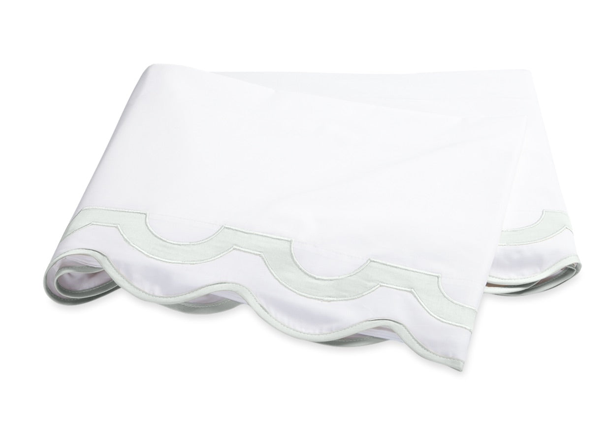 Showcasing the Mirasol Bedding Collection by Matouk, this folded white sheet features elegant scalloped edges and delicate light green trim, expertly crafted from luxurious Egyptian cotton percale with a 600 thread count, displayed against a plain white background.