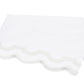 A folded white towel with scalloped edges and a light gray trim, from the Matouk Mirasol Bedding Collection, crafted from luxurious 600 thread count Egyptian cotton percale, placed on a plain white background.