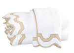 Two folded white towels with beige scalloped trim from the Matouk Mirasol Bath Collection are stacked on a white surface.