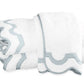 A stack of folded Mirasol Bath Collection towels by Matouk, crafted from white Cairo cotton terry with light blue trim, arranged on a plain white background.