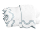 A stack of folded Mirasol Bath Collection towels by Matouk, crafted from white Cairo cotton terry with light blue trim, arranged on a plain white background.