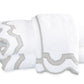 Two folded white towels from the Matouk Mirasol Bath Collection feature decorative scalloped edges trimmed in light gray and are stacked on a white background.