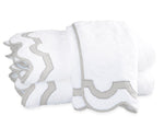 Two folded white towels from the Matouk Mirasol Bath Collection feature decorative scalloped edges trimmed in light gray and are stacked on a white background.