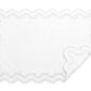 A white rectangular bath mat with scalloped edges and a raised border, inspired by the Matouk Mirasol Bath Collection. One corner is slightly folded over, showcasing the elegant Matouk design details.