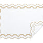 The Matouk Mirasol Bath Collection features a white rectangular bath mat with a scalloped beige border, folded corner, and elegant reversible pattern, designed to coordinate with Matouk’s Cairo cotton terry towels.