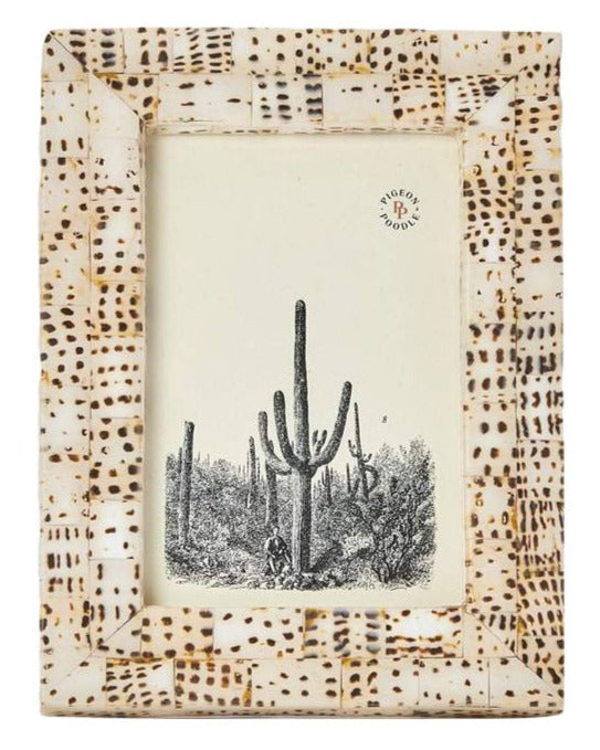 The Mombasa Frame Collection by Pigeon & Poodle features a rectangular photo frame in smooth resin with a beige and brown dotted pattern, shown displaying a black and white illustration of cacti and a small human figure.