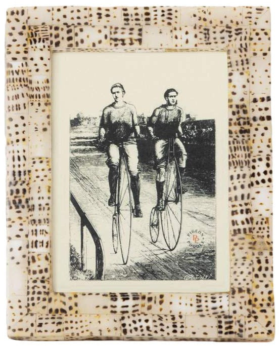 Black-and-white illustration of two riding vintage high-wheel bicycles, showcased in a Mombasa Frame Collection rectangular frame by Pigeon & Poodle featuring a subtle subway tile pattern.