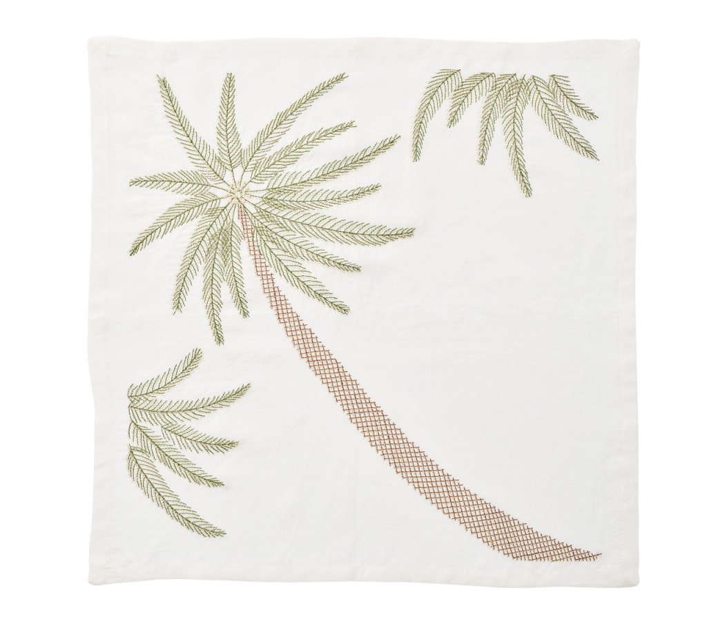 The Kim Seybert Palm Coast Napkin Set features white cloth napkins embroidered with palm fronds and a tall palm tree, adding a coastal touch to your dining table.
