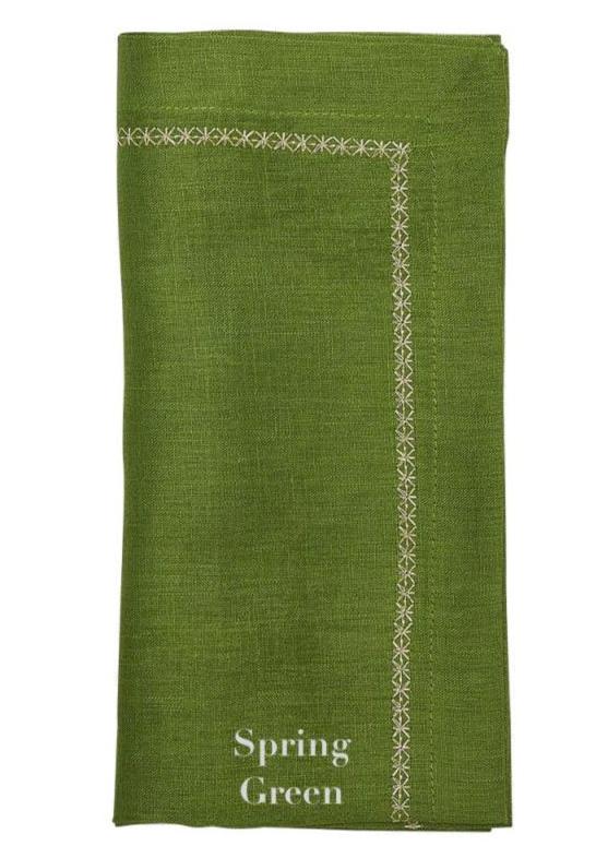 A folded green linen napkin from the Kim Seybert Classic Napkin Set, labeled "Spring Green," features a classic embroidered border design.