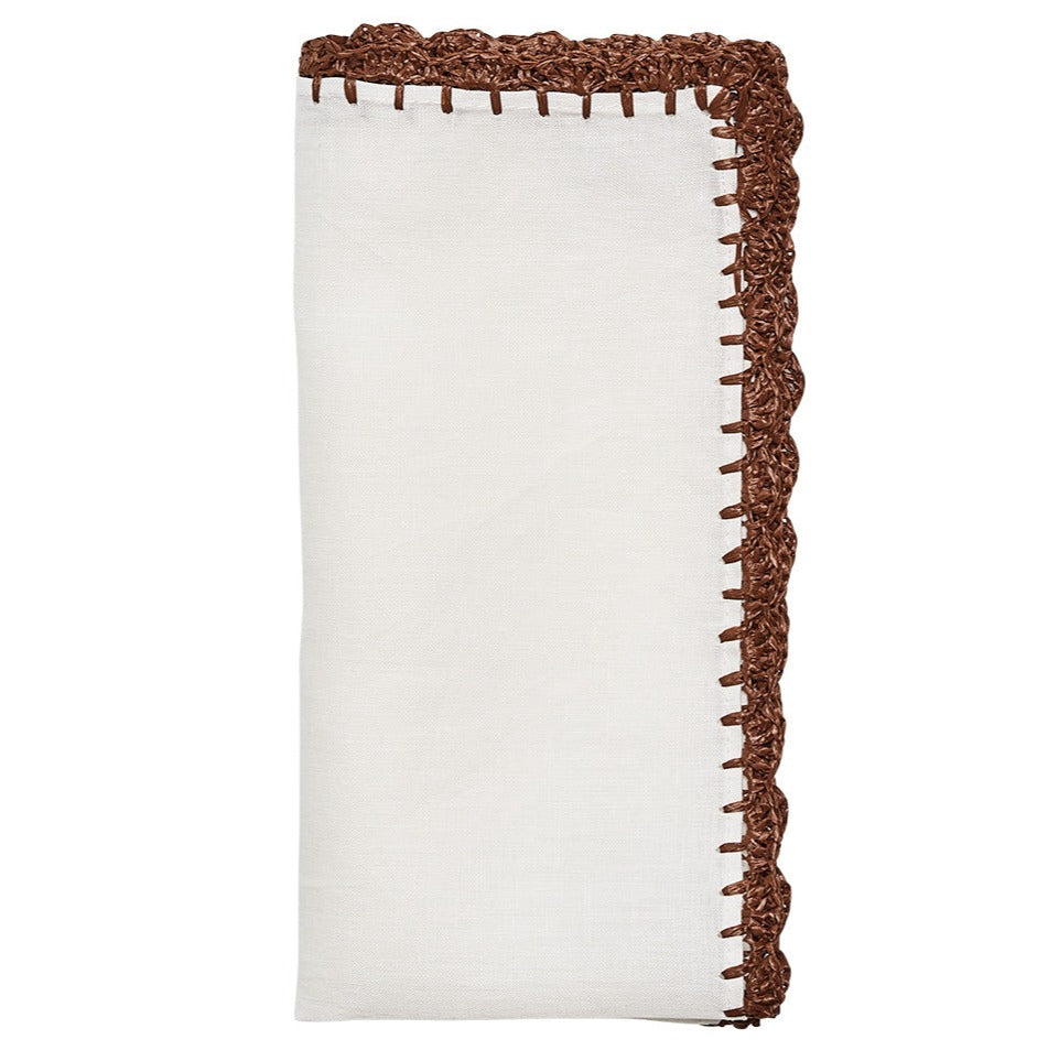 The Kim Seybert Shell Edge Napkin Set features folded white linen napkins with brown crochet trim, adding charm to any bohemian table setting.