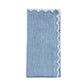 The Arches Napkin Set by Kim Seybert features four folded blue linen napkins with white lace trim along one edge, displayed against a white background.