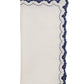 The Arches Napkin Set by Kim Seybert features folded white linen napkins with dark blue scalloped, embroidered edges and a subtle geometric design.