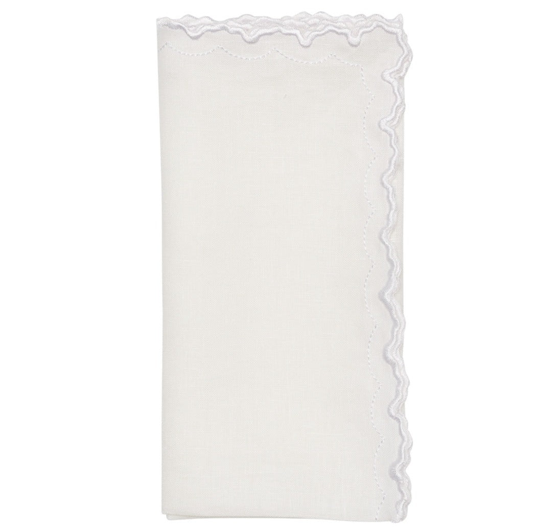 The Arches Napkin Set by Kim Seybert features folded white linen napkins with a geometric design and a scalloped, embroidered edge on one side, shown against a plain white background.