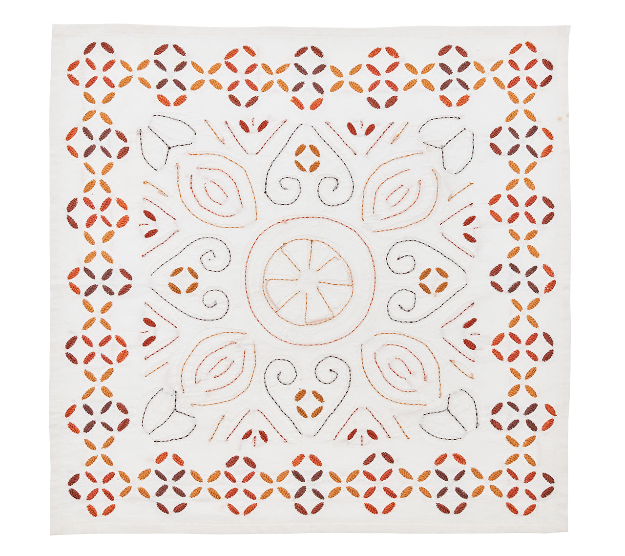 The Malta Napkin Set by Kim Seybert features square white napkins with symmetrical, hand-stitched geometric and floral patterns in orange, brown, and yellow, celebrating traditional cutwork techniques.