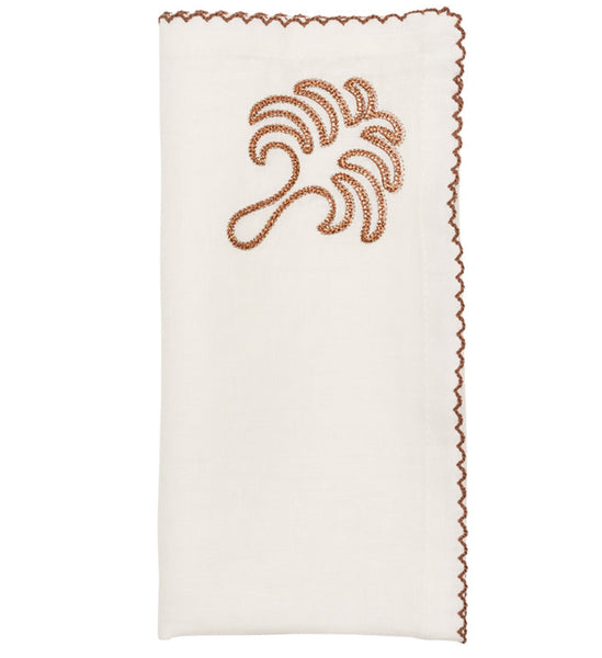 The Kim Seybert Royal Palm Napkin set includes four white linen napkins with a hand-embroidered abstract design, featuring a brown tropical leaf motif and matching scalloped edges.