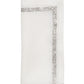 The Kim Seybert Impression Napkin Set features white linen napkins with a subtle silver embroidered border, neatly folded against a plain background.
