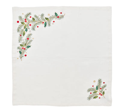 The Christmas Carol Table Linen Collection by Kim Seybert features a white cloth napkin embroidered with green pine branches and red-gold berries in two corners, ideal for festive holiday table settings.