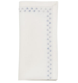 The Starry Night Napkin Set by Kim Seybert features folded white linen napkins with shimmering metallic blue floral embroidery along the border, adding a delicate, elegant touch to any table setting.