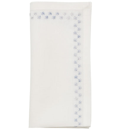 The Starry Night Napkin Set by Kim Seybert features folded white linen napkins with shimmering metallic blue floral embroidery along the border, adding a delicate, elegant touch to any table setting.