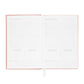 An open Flax Gratitude Journal by Sugar Paper displays two pages with prompts for gratitude, intentions, and daily actions, featuring lined sections for writing. This journal includes a daily check-in and is finished with a pink cover and white ribbon bookmark.