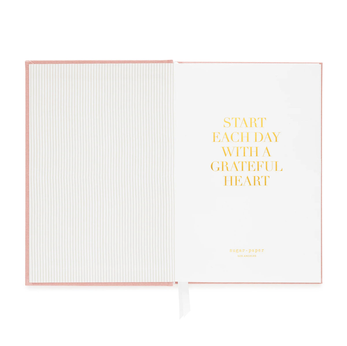Introducing the Sugar Paper Flax Gratitude Journal: This open pink notebook showcases a striped inner cover and a white page adorned with gold text reading, “Start each day with a grateful heart.” Perfect for your daily check-in or as a gratitude journal, it features thoughtful prompts and includes a white ribbon bookmark.