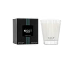 The Nest Forest Rain Scent Collection candle, displayed in a textured clear glass holder beside its black box, fills the space with an aquatic fragrance layered with subtle fig leaf notes.