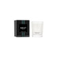 A Nest Forest Rain Scent Collection candle with fig leaf notes rests in a clear glass holder next to its black box adorned with teal and white stripes.