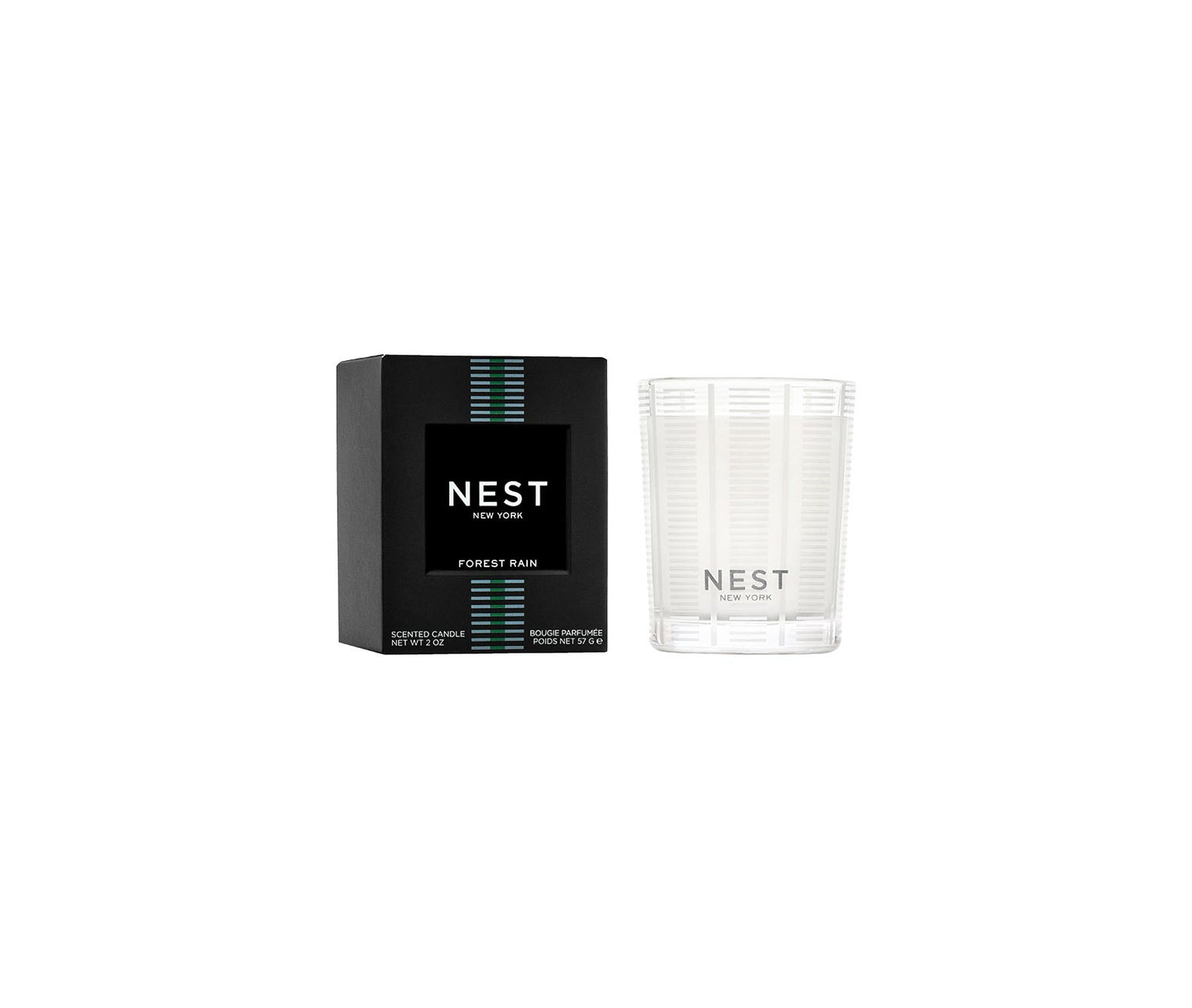 A Nest Forest Rain Scent Collection candle with fig leaf notes rests in a clear glass holder next to its black box adorned with teal and white stripes.