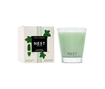 Nest's Cucumber & White Sage Scent Collection candle features a refreshing wellness fragrance and is pictured beside its white box decorated with green plant illustrations.