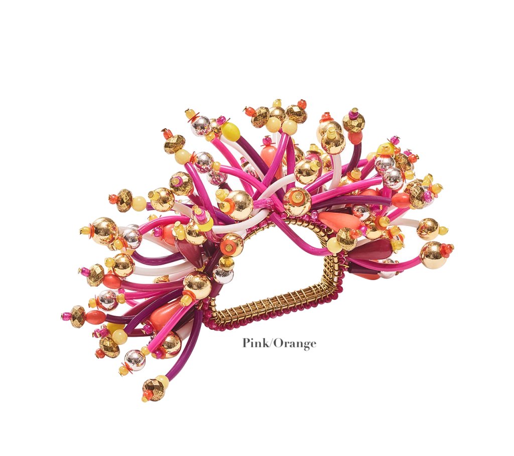 The Kim Seybert Fun Burst Napkin Ring features pink and orange flexible silicone tubes, gold and silver metallic beads, displayed with the label "Pink Orange" on a white background.
