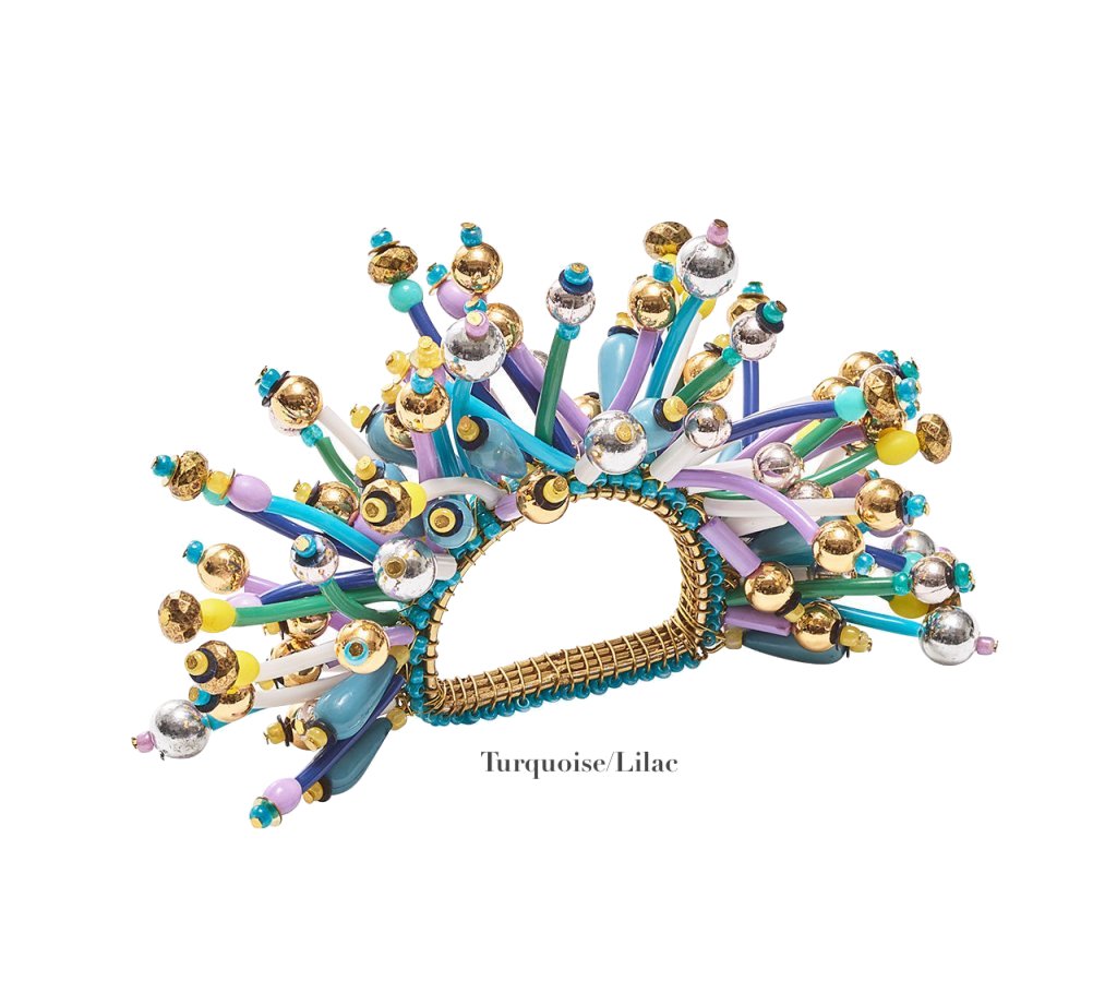 The Kim Seybert Fun Burst Napkin Ring features gold, turquoise, lilac, and silver metallic beads on spiky strands in an arc with silicone tube accents for a modern touch. The text reads "Turquoise/Lilac.