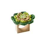 The Kim Seybert Pareo Napkin Ring features a decorative green and beige raffia-style flower made from woven material attached to a wooden ring.