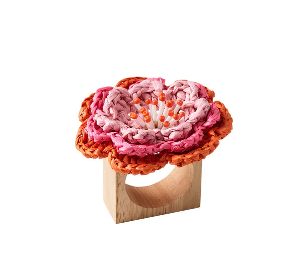 The Kim Seybert Pareo Napkin Ring features a wooden base topped with a raffia-style woven flower in pink and orange shades, accented with white and orange at the center.