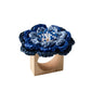 The Pareo Napkin Ring by Kim Seybert features a square wooden base topped with a blue hand-crocheted flower, bringing unique artisanal charm to your table setting.